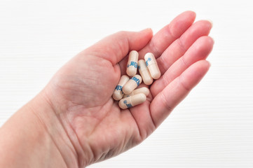 Female hand holding many colorful pills, capsules, tablets on white wooden background.Taking Your Medication.Top view.