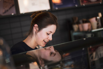 smiling mature female staff offering fresh pastry in sweet-shop. selective focus, noise effect