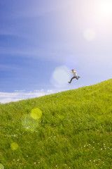Happy man running and jumping in bright green field with blue sky