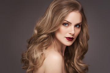 Naklejka premium Young brown-haired woman with long curly hair. Beautiful face of gorgeous girl with blue eyes. Nice portrait of a caucasian female looking at camera. Attractive fashion model