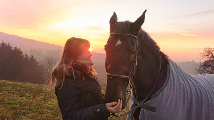 Obraz premium SUN FLARE: Loving young woman looks at and caresses the beautiful female horse.