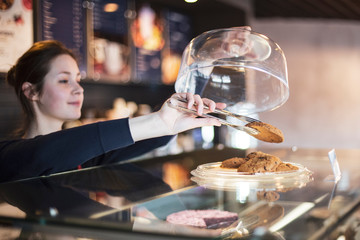 happy woman or waitress with cakes and tongs at cafe counter. small business, food, people and service concept, selective focus, noise effect