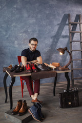 attractive shoemaker sitting at the table with repaired shoes in the work shop with blue wall, hobby, profession