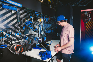 Theme business profession manager and technology. Young stylish Caucasian male owner bicycle shop uses a laptop computer near the stand with the tools for repairing and servicing the bicycle