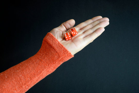Red playing dices in a male hand pointing up on black background, closeup, selective focus.