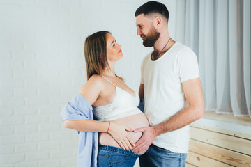 Fototapeta premium a pregnant girl is hugged by her husband at the girl's bare stomach, red ribbons from the evil eye on her hands