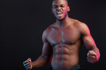 Fototapeta na wymiar Attractive African male fighter or boxer posing shirtless, isolated over dark background. Toned and ripped muscular fitness man under dramatic low key lighting, copy space.