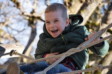 cheerful boy on a child's coat climbing on the ropes