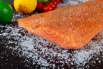 Preparing raw salmon fillet with lemon on a dark slate plate, view from above. Vegetarian food concept.