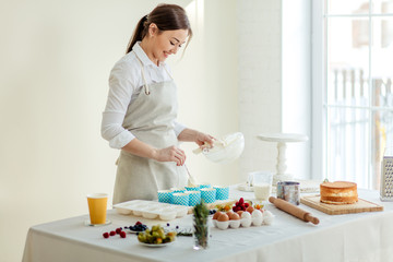 cheerful beautiful female chef using the spoon to scoop cupcake batter, close up side view photo. copy space