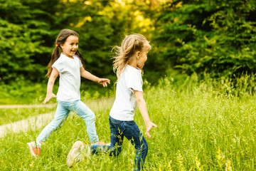 Two sisters run through the forest holding hands. Summer sunny day and girls. Beautiful long hair in a child
