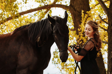 Fototapeta premium pretty woman with black horse in autumnal nature. Fashion photoshoot