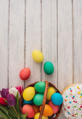Fototapeta na wymiar Colorful easter eggs,cake,spring tulips on wooden texture background.On a white wood table,colored eggs,flowers,bread.Happy religious day,traditional for people. Top view.Copy space.