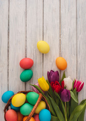 Fototapeta na wymiar Colorful easter eggs,spring tulips on wooden texture background.On a white wood table,colored eggs,colors flowers.Happy religious day,traditional for people. Top view.Copy space.
