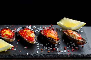 Fresh oysters are laid out on black slate, coarse salt is sprinkled around. Seafood.