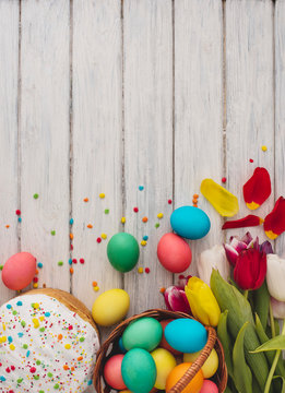 Colorful easter eggs,cake,spring tulips  on wooden texture background.On a white wood table,colored eggs,flowers,bread.Happy religious day,traditional for people. Top view.Copy space.