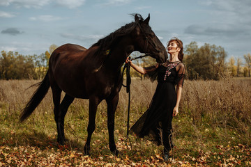 pretty woman with black horse in autumnal nature. Fashion photoshoot