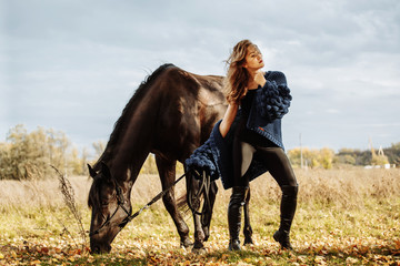 pretty woman with black horse in autumnal nature. Fashion photoshoot