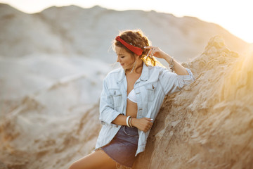 A pretty girl in jeans, short shorts, a red hoop and a white bra is sitting on the sand by the sea...