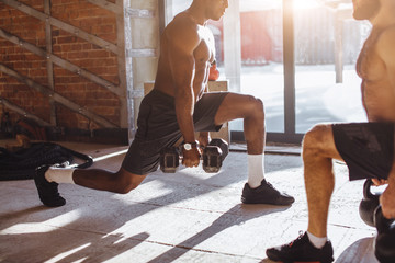 Two multiracial male crossfit sportsmen with naked torso, exercising actively in sunny morning...