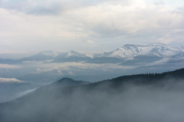 Magic spring fogs in Ukrainian Carpathians overlooking the snow-capped mountain peaks from the picturesque mountain valley with tourists in tents.