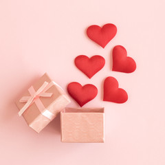 Flat lay of gift box and hearts against pastel pink background.