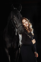Fototapeta na wymiar Portrait of young pretty woman and black horse on black background isolated. Fashion concept