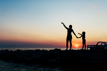 Fototapeta premium Mom and daughter spend time at the sea in the background of the sunset