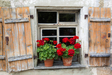 Fototapeta na wymiar Altes Fenster mit offenen Holzfensterläden und Blumenkästen mit Geranien
