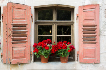 Fototapeta na wymiar Altes Fenster mit offenen Holzfensterläden und Blumenkästen mit Geranien