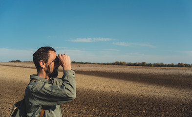 Man in the field looks through binoculars