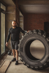 Obraz na płótnie Canvas CrossFit Tire Technique. Powerful bodybuilder explains rules and order of training with improvised powerlifting element, standing near huge tire in fitness club