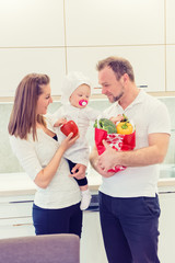 Happy parents standing in the kitchen and prepares for cooking with their baby girl chef. Father bring vegetables in paper bag.