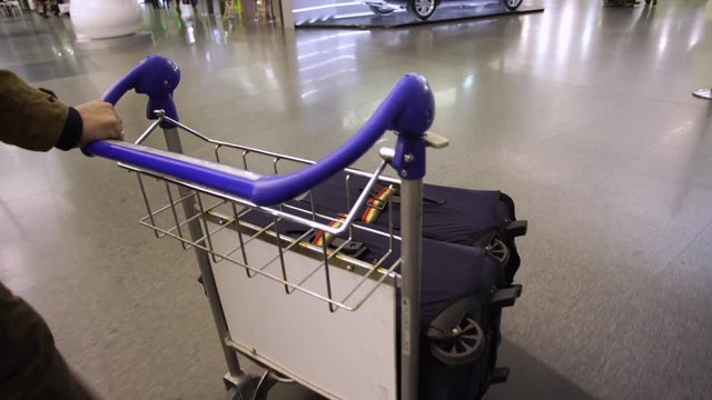 Person transporting his baggage using trolley at airport. 2 blue suitcases laying on trolley.