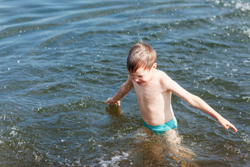Joyful boy swimming in the lake and splashing in the water. Boy play in water in summer. 