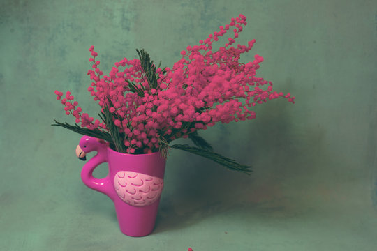 Pink mug or flower pot of flamingo shape with pink mimosa on a dark emerald green background