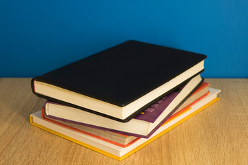 stack of books lying on top of each other wooden surface blue background