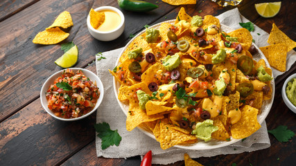 Mexican nachos tortilla chips with olives, jalapeno, guacamole, tomatoes salsa, cheese dipand beer.