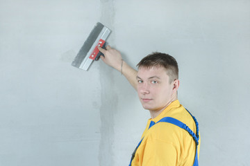 House painter plasters walls. Repairman holds a spatula in his hands. A man in work clothes.