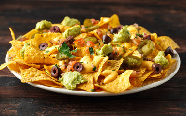 Mexican nachos tortilla chips with olives, jalapeno, guacamole, tomatoes salsa and cheese dip. close up