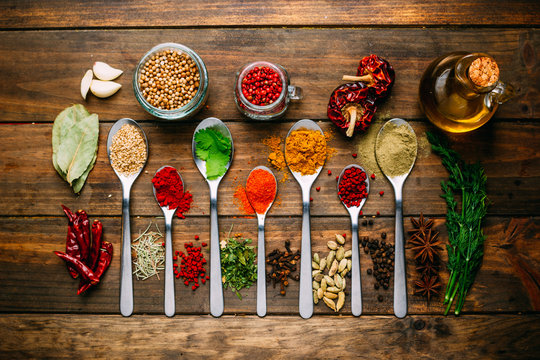 Bunch of assorted spices placed in order on lumber tabletop near bottle of oil