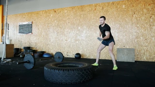 Muscular man hitting tire with a hammer, fitness concept in slow motion.