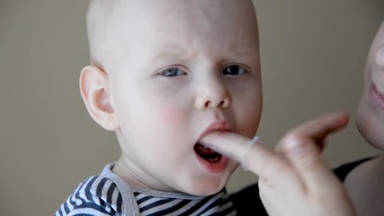 Mom brushes baby's teeth with a silicone brush that fits on her finger