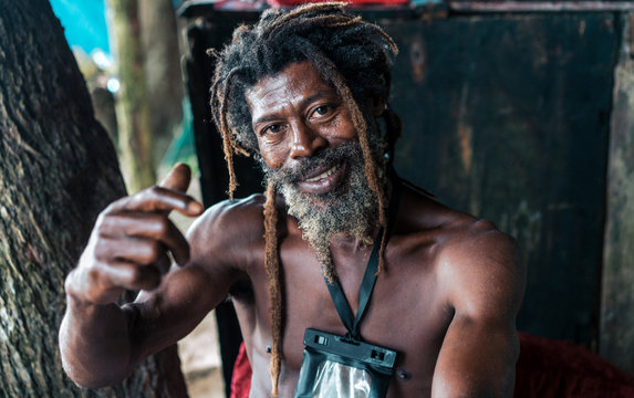 African American bearded male with dreadlocks and upped hands smoking cigar near trees