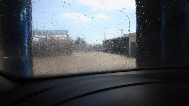 Puente de lavado de coches automatico en el proceso de rociar con agua y espuma de jab&oacute;n. Comenzando a girar los rodillos sobre el parabrisas. Visto desde el interior del automovil 