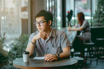 Asian guy with glasses sitting and writing something with thought.