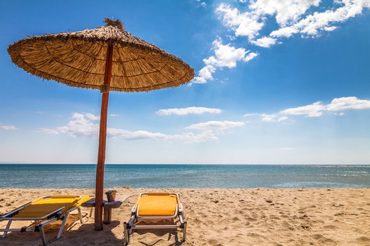 A straw umbrella with deck chairs on a sandy beach by the sea. The Paralia, a tourist seaside part of the municipality Katerini, Greece, Europe.