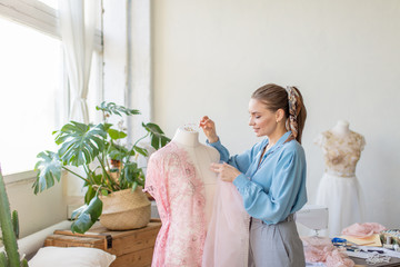 Portrait of a caucasian attractive dressmaker creating a wedding dress of a lace fabric. Exclusive...
