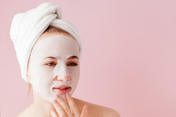 Beautiful young woman is applying a cosmetic tissue mask on a face on a pink background