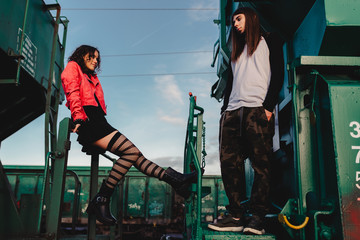 Side view of young hipsters in trendy wear standing on old locomotive on railroad